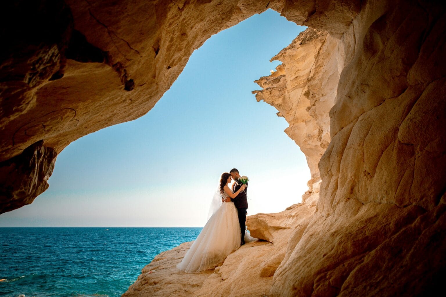 Travel agency - the bride and groom hug each other in a rocky beach environment, celebrating their wedding day with a picturesque view. Planning a honeymoon trip to various romantic destinations.
