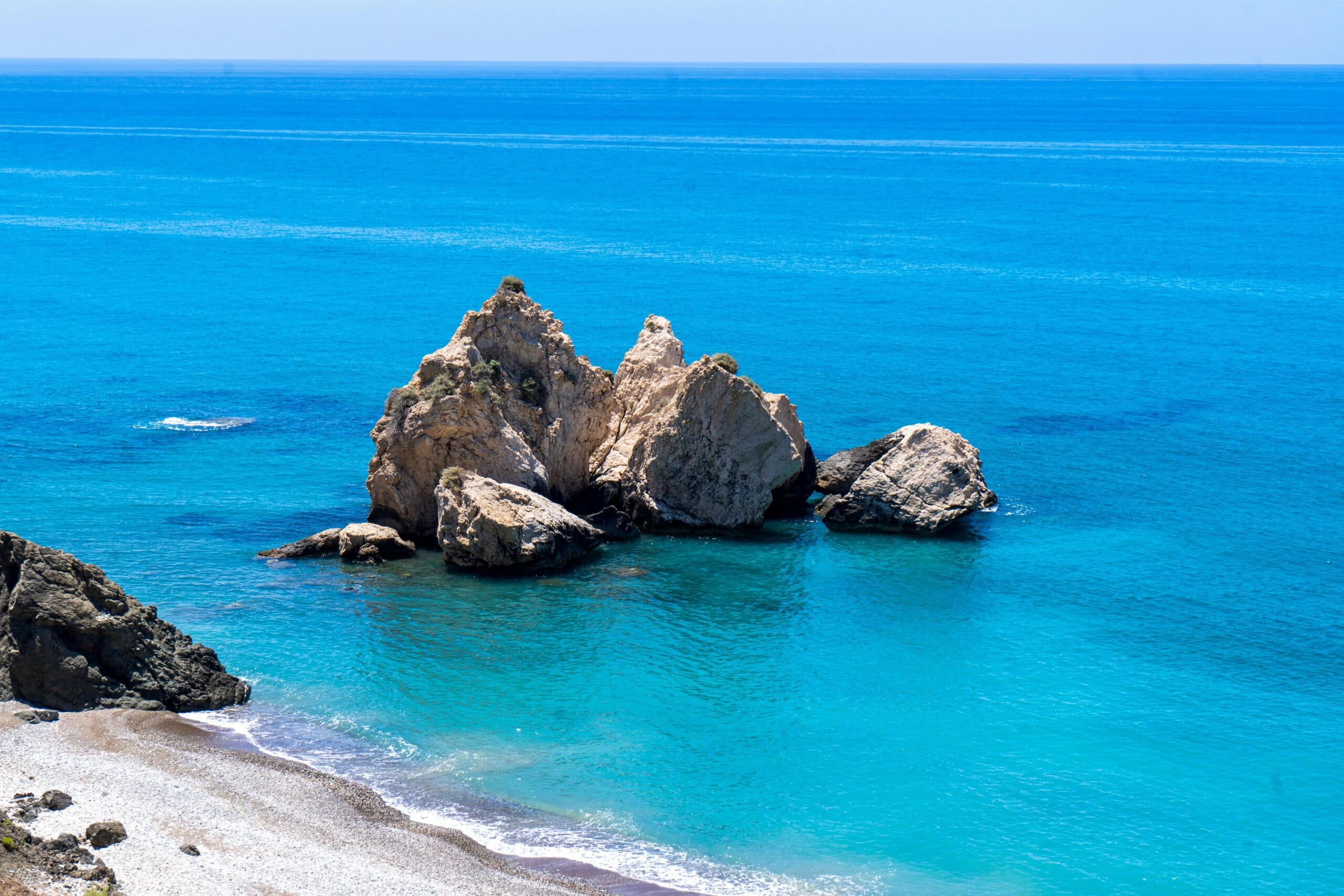 נוף ימי אידילי בפטרה טו רומיו בפאפוס, קפריסין, עם מים תכולים והתצורות הסלעיות.