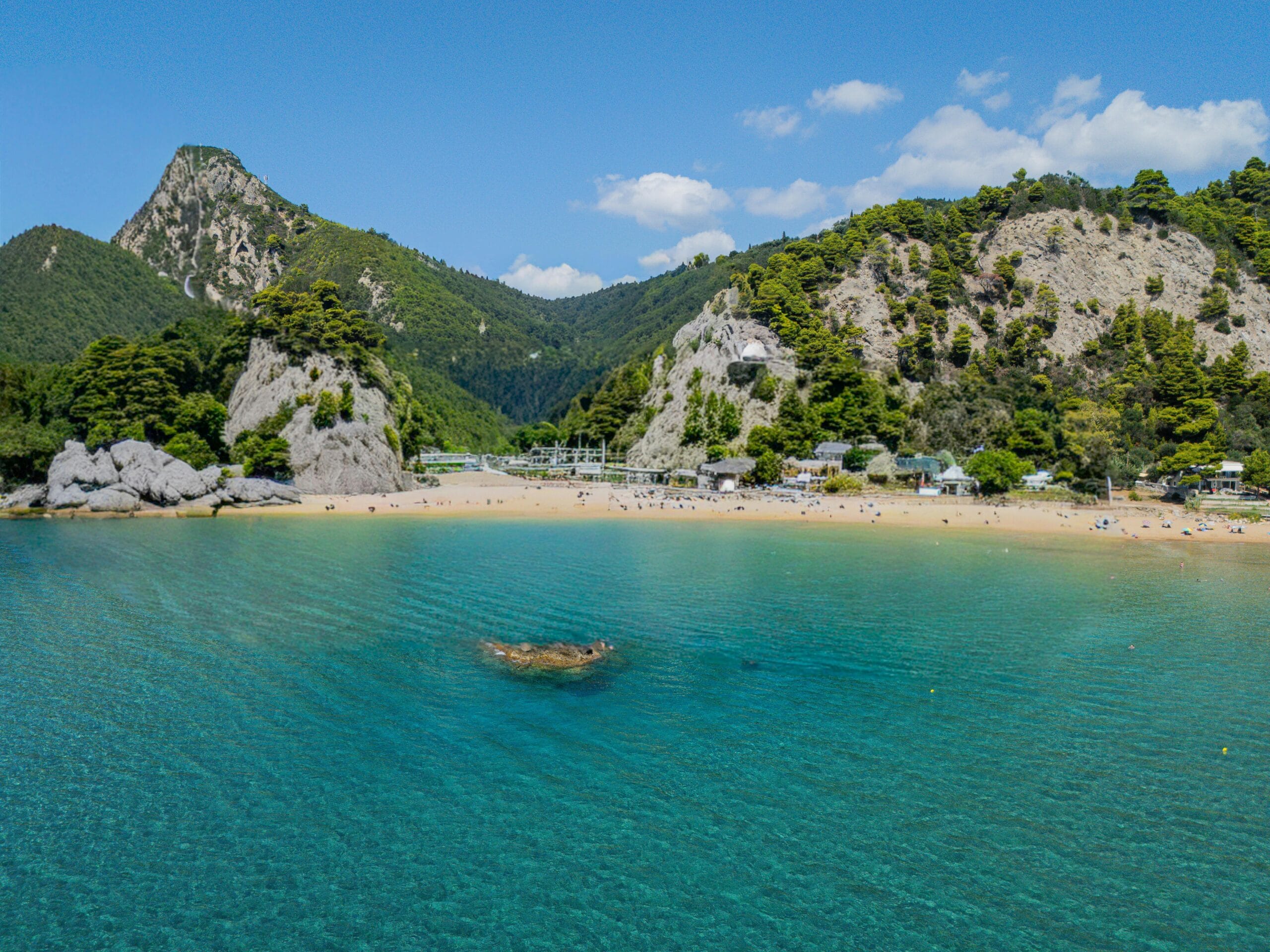 חוף ים עם מי טורקיז לרקע נוף ההרי ירוק ומסולע