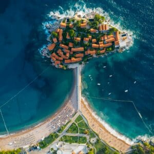 תמונה אווירית מהממת של אי חופי עם מים בירוק טורקיז ובניינים עם גגות צבעוניים בעיירה בלקנית