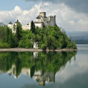 טירת נדזיצה המשתקפת על אגם שקט מוקף בירק שופע.